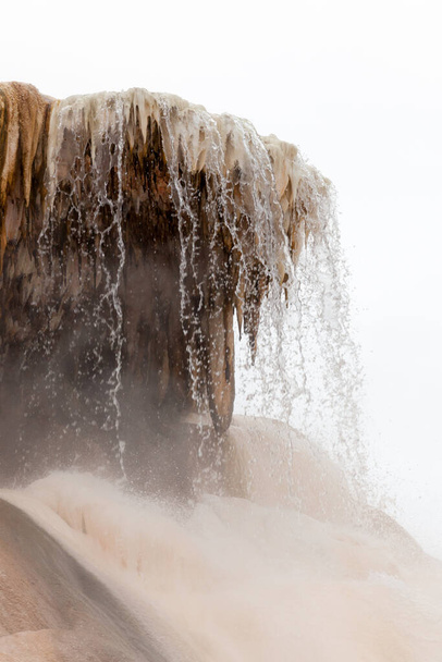 Cascatas de água quente de um travertino com estalactites penduradas e vapor quente flutuando em Mammoth Hot Springs, Wyoming
. - Foto, Imagem