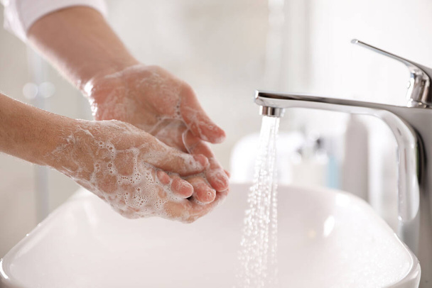 Man washing hands with soap over sink in bathroom, closeup - Foto, afbeelding