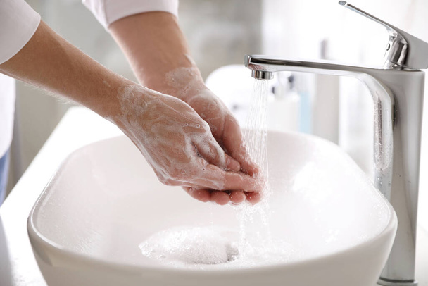Man washing hands with soap over sink in bathroom, closeup - 写真・画像