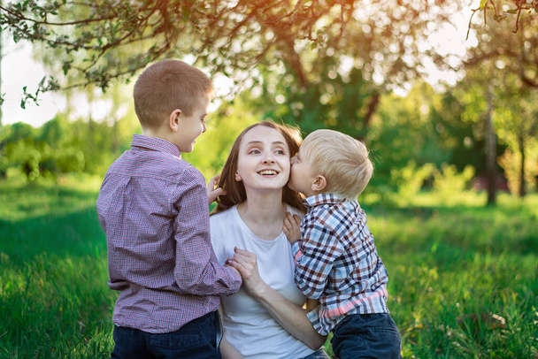 Mutter mit zwei Söhnen im Park. Kind küsst seine Mutter. Glückliche Mutterschaft. - Foto, Bild