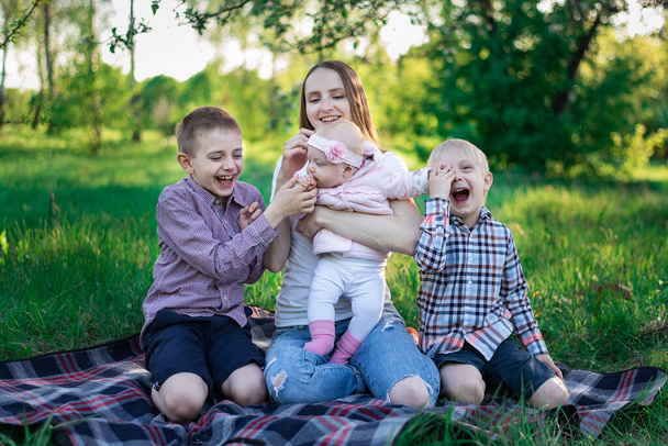 Anya két fiával és kislányával a pikniken. Három gyerek és anya a természetben. Nagy család. - Fotó, kép