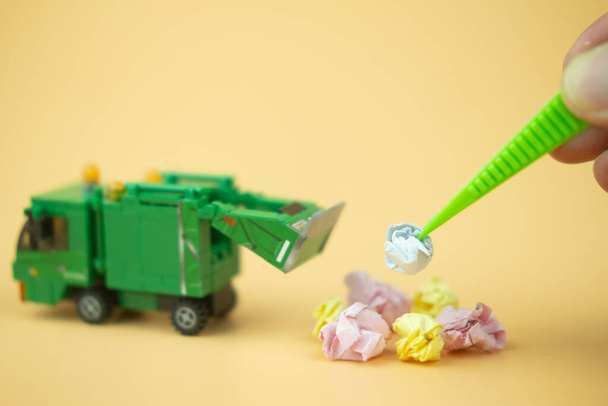 Pince à épiler en plastique à la main mettant du papier froissé dans un camion à ordures sur fond jaune
 - Photo, image