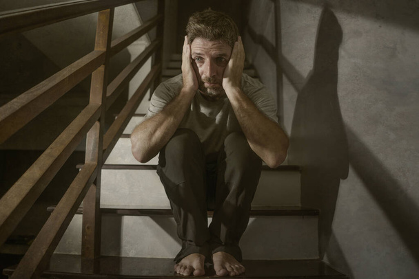 horror movie style portrait of sad and desperate man suffering depression problem or mental disorder sitting on staircase at home hopeless crying overwhelmed and helpless - Foto, afbeelding