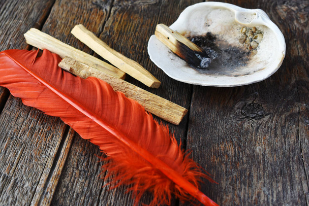 古い木のテーブルの上に明るいオレンジ色の羽でパロ・サント・スマッジの棒のイメージ. - 写真・画像
