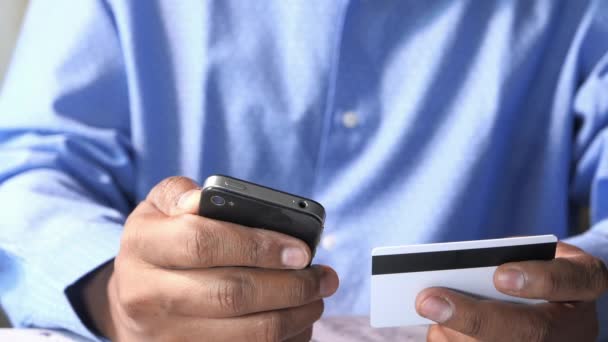 Manos de hombre sosteniendo una tarjeta de crédito usando un teléfono inteligente para compras en línea
 - Imágenes, Vídeo