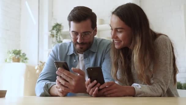 Gelukkig familie paar zitten aan houten tafel, met behulp van smartphones. - Video