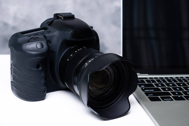 Μια μαύρη ψηφιακή κάμερα και ένα φορητό υπολογιστή σε ένα τραπέζι - Φωτογραφία, εικόνα