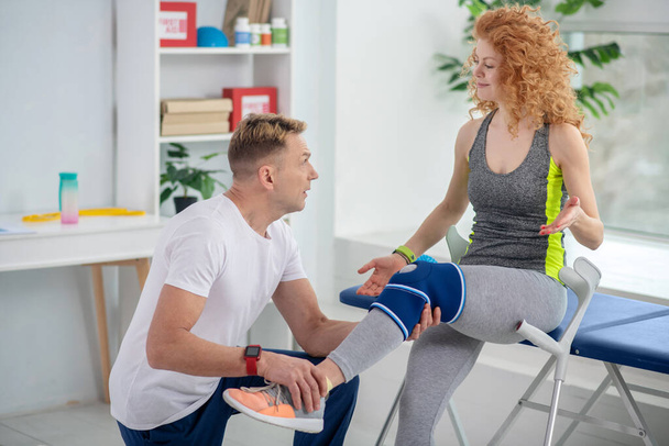 Male physiotherapist holding leg of female patient sitting on couch - Φωτογραφία, εικόνα