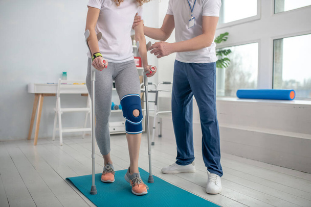 Male physiotherapist helping female patient walk with crutches - Zdjęcie, obraz