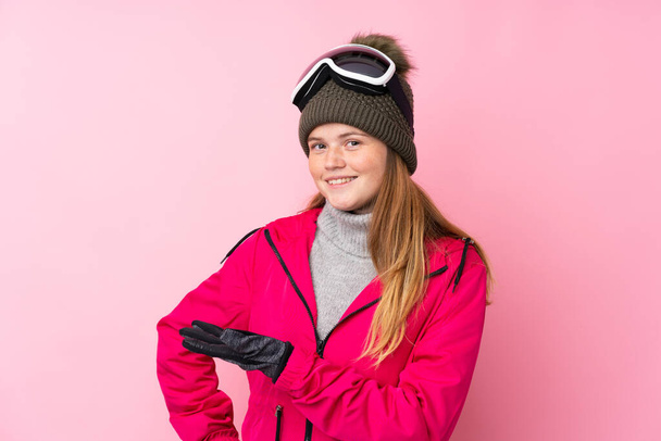 Menina adolescente ucraniana esquiador com óculos de snowboard sobre fundo rosa isolado estendendo as mãos para o lado para convidar para vir
 - Foto, Imagem