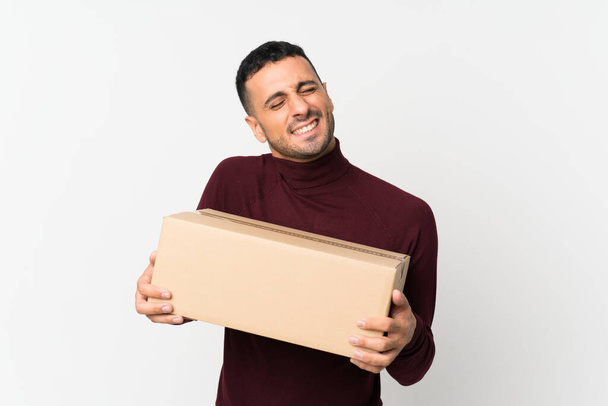 Mladý muž na izolovaném bílém pozadí drží krabici přesunout na jiné místo - Fotografie, Obrázek