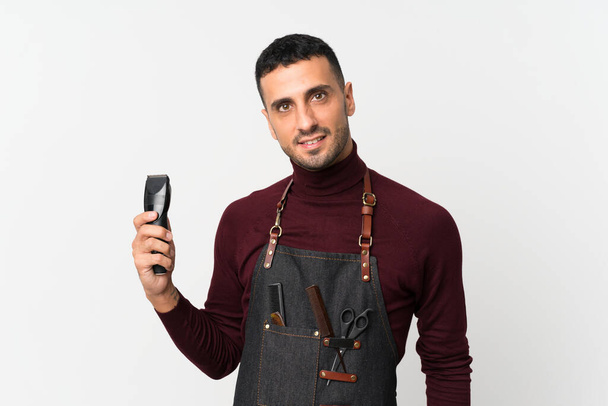 Young man over isolated white background with hairdresser or barber dress and holding hair cutting machine - Photo, Image