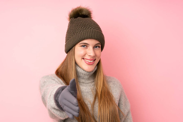 Junges Teenager-Mädchen mit Wintermütze über isoliertem rosa Hintergrund beim Händeschütteln nach einem guten Geschäft - Foto, Bild