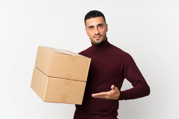 Молодой человек на изолированном белом фоне держит коробку, чтобы переместить ее на другое место
 - Фото, изображение