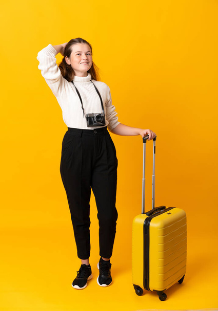 Full body of traveler teenager girl with suitcase over isolated yellow background laughing - Photo, Image