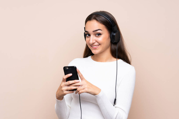 Young woman over isolated background using the mobile with headphones - Photo, Image
