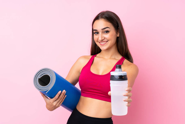 Young sport girl over isolated pink background with sports water bottle and with a mat - Fotografie, Obrázek