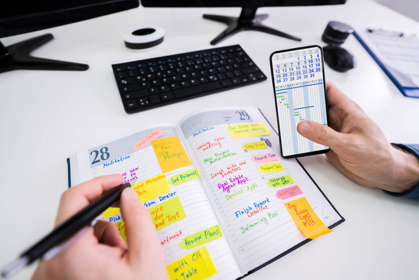 Close-up Of A Businessman Holding Cellphone Writing Schedule In The Diary With Pen - Photo, Image