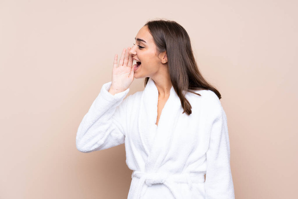 Молодая девушка в халате на изолированном фоне кричит с открытым ртом - Фото, изображение