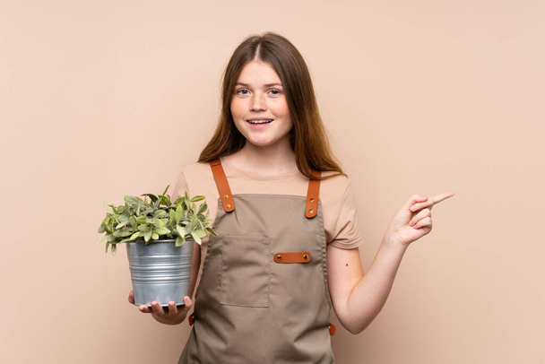 Українська дівчина - садівник, що тримає рослину, показуючи пальцем на бік. - Фото, зображення