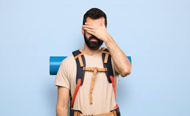 Hiker man covering eyes by hands. Do not want to see something over isolated blue background - Photo, Image