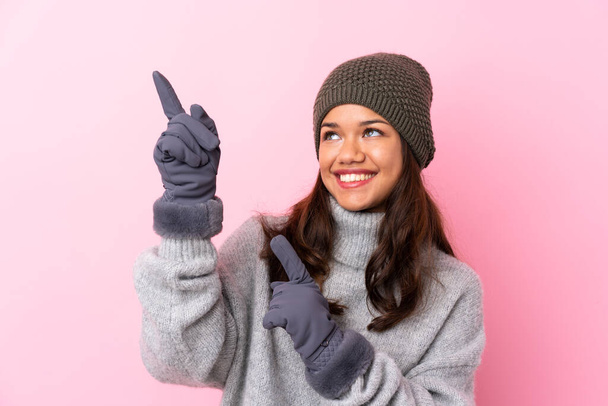 Young Colombian girl with winter hat over isolated pink wall pointing with the index finger a great idea - Photo, Image