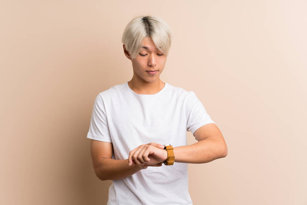Young asian man over isolated background with wrist watch - Фото, изображение