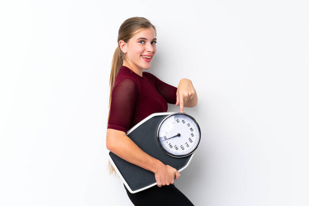 Teenager girl with weighing machine over isolated white background holding a weighing machine and pointing it - Фото, зображення