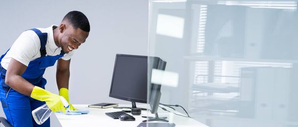 オフィスで羽ダスター付き若い男性メイドクリーニングガラスデスク - 写真・画像