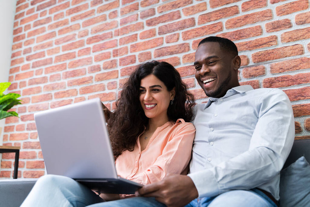Portrait Of A Happy Young Couple Sitting On Couch Using Laptop - Photo, Image