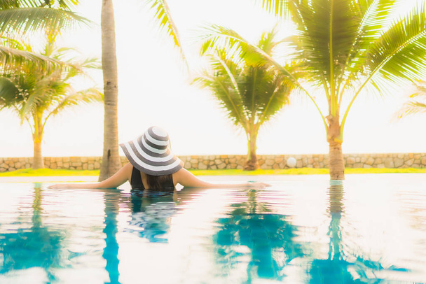 Retrato hermosa mujer asiática joven relajarse alrededor de la piscina al aire libre en el complejo hotelero con palmera al atardecer o al amanecer para vacaciones de ocio - Foto, Imagen