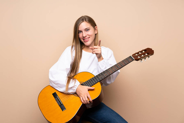 Teenager-Mädchen mit Gitarre über isoliertem Hintergrund zeigt mit selbstbewusstem Gesichtsausdruck auf dich - Foto, Bild