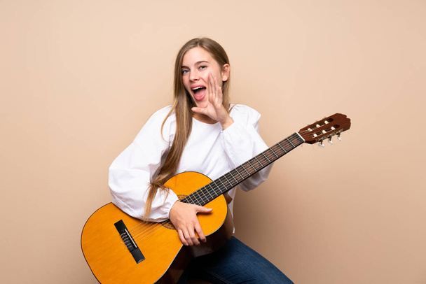 Teenager girl with guitar over isolated background shouting with mouth wide open - Foto, Bild