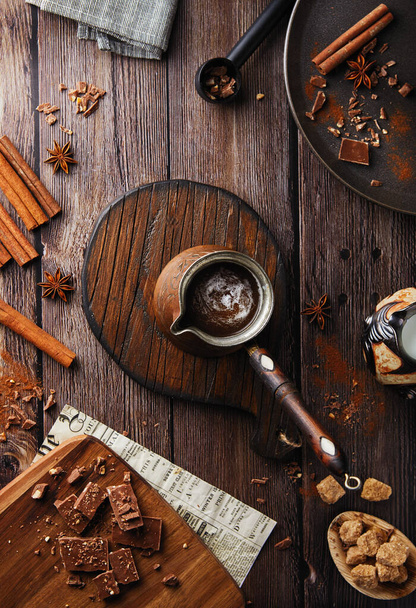Ploché kakao leželo na venkovském pozadí. Samičí ruka drží Turku s dřevěnou rukojetí kakaové čokolády s teplým nápojem na dřevěném stole, útulným pozadím, čokoládou a skořicí, slavnostní kavárnou - Fotografie, Obrázek