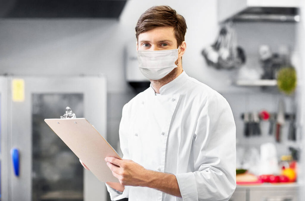 chef with clipboard in face mask at restaurant - Foto, Imagen