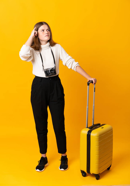 Sarı arka planda bavulu olan gezgin bir genç kızın tüm vücudu şüphe ve kafa karıştırıcı bir ifadeyle dolu. - Fotoğraf, Görsel