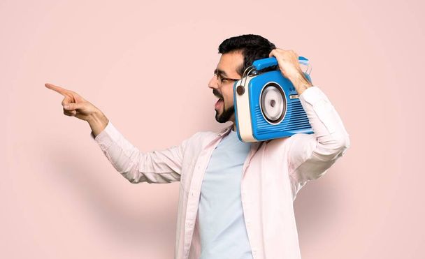 Όμορφος άντρας με γενειάδα κρατώντας ένα ραδιόφωνο πάνω από απομονωμένο ροζ φόντο - Φωτογραφία, εικόνα