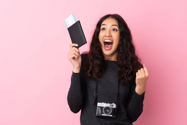 Gemischte Rassenfrau vor isoliertem rosa Hintergrund glücklich im Urlaub mit Pass und Flugtickets - Foto, Bild