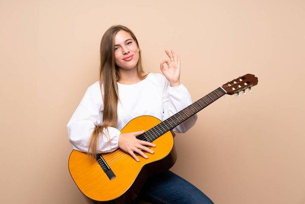 Teenager girl with guitar over isolated background showing ok sign with fingers - Фото, изображение