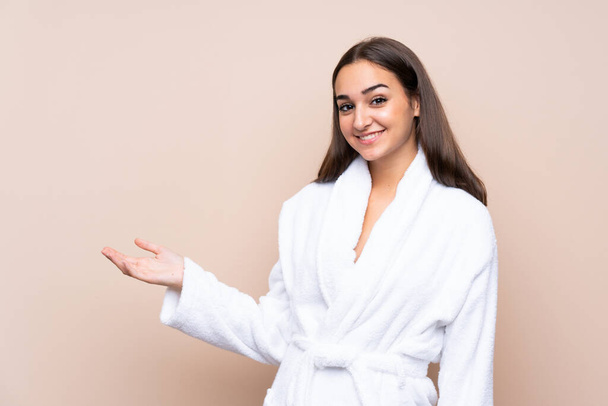 Young girl in a bathrobe over isolated background holding copyspace imaginary on the palm - Foto, Imagem