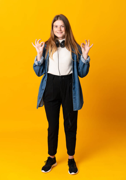 Student ukrainian teenager girl over isolated yellow background showing an ok sign with fingers - Foto, afbeelding