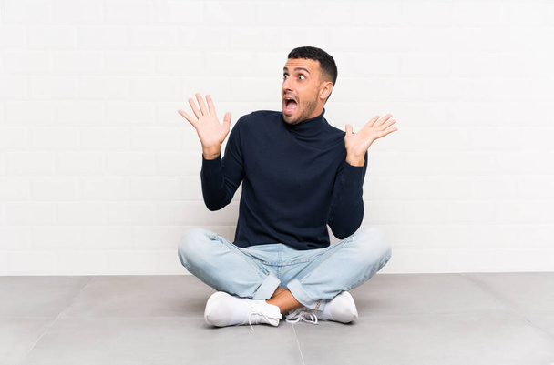 Young handsome man sitting on the floor with surprise facial expression - Photo, Image