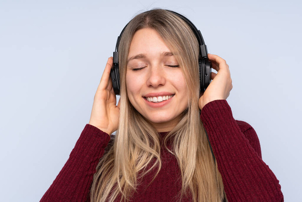 Jonge blonde vrouw over geïsoleerde blauwe achtergrond luisteren muziek - Foto, afbeelding