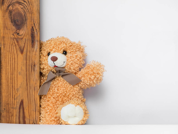Teddy bear hides over the wooden door, white background; fragment of a childish decor - Foto, Imagem