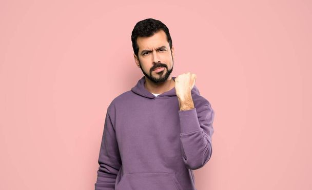 Όμορφος άνδρας με φούτερ με θυμωμένη χειρονομία πάνω από απομονωμένο ροζ φόντο - Φωτογραφία, εικόνα