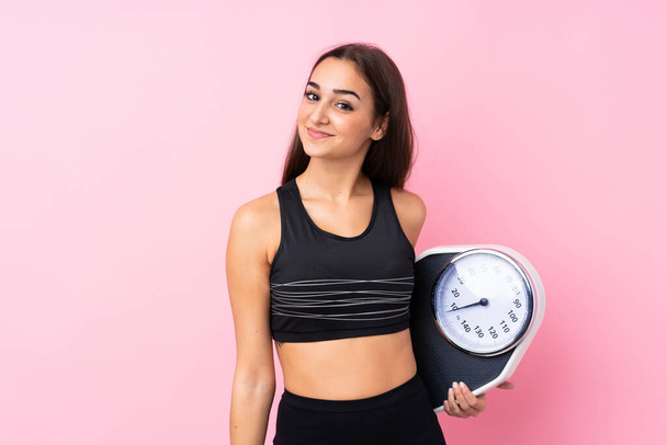 Pretty young girl with weighing machine over isolated pink background with weighing machine - Foto, immagini