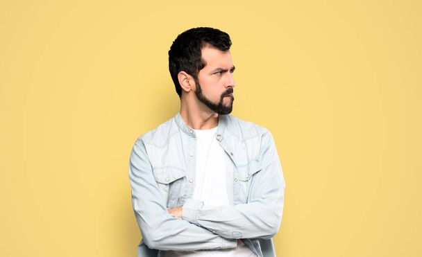 Handsome man with beard with confuse face expression over isolated yellow background - Foto, afbeelding
