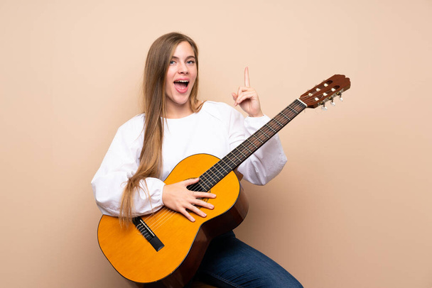 Chica adolescente con guitarra sobre fondo aislado apuntando a una gran idea
 - Foto, imagen