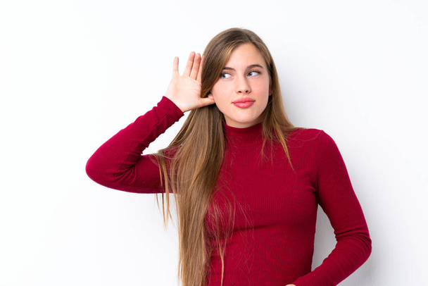 Adolescente loira sobre isolado fundo branco ouvindo algo, colocando a mão na orelha
 - Foto, Imagem