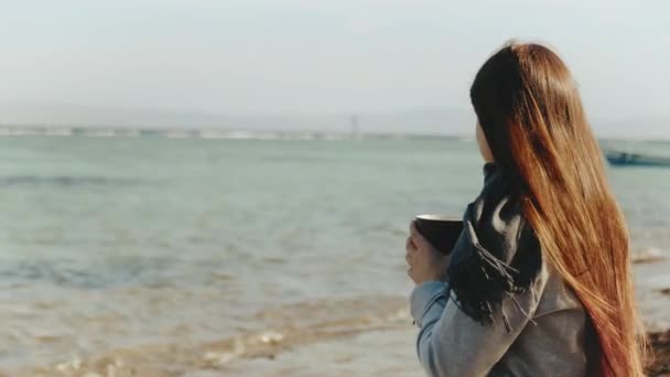 Kobieta pije kawę lub herbatę na plaży z niebieskim widokiem na morze, kobieta patrzy w horyzont, szybki film, zwolnione tempo, 4k - Materiał filmowy, wideo